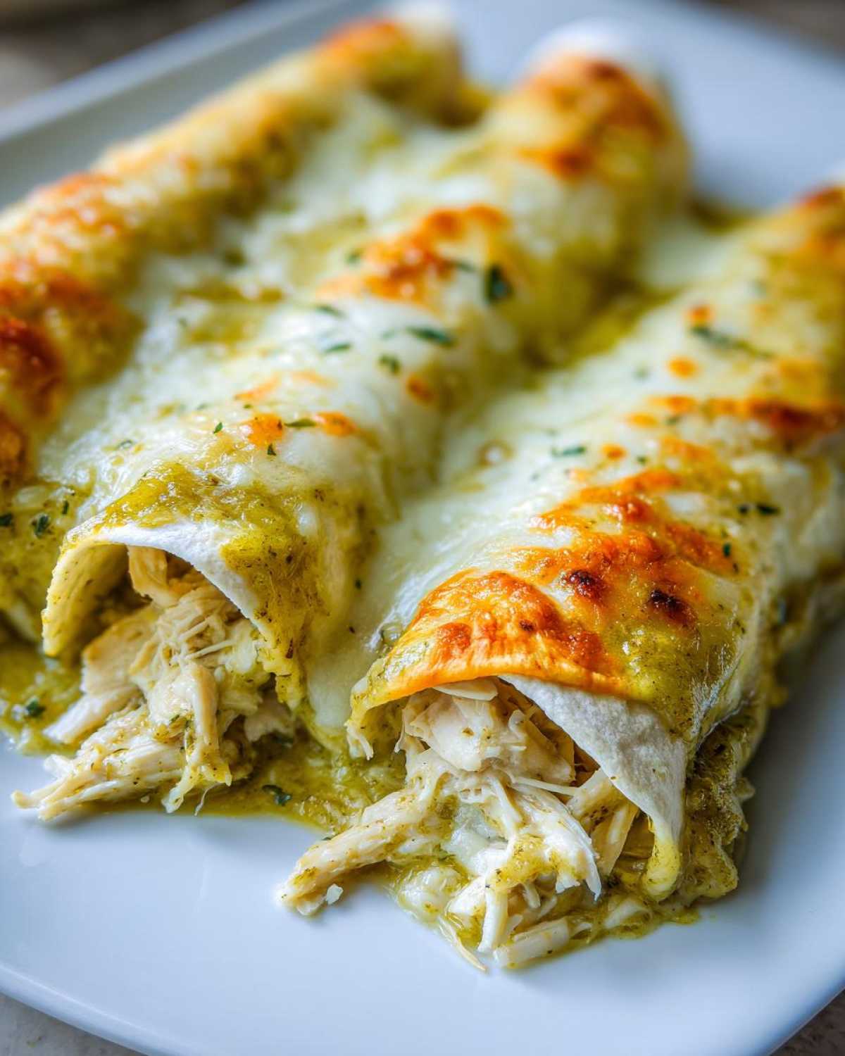 Close-up of three delicious green chile chicken enchiladas covered in melted, slightly browned cheese.