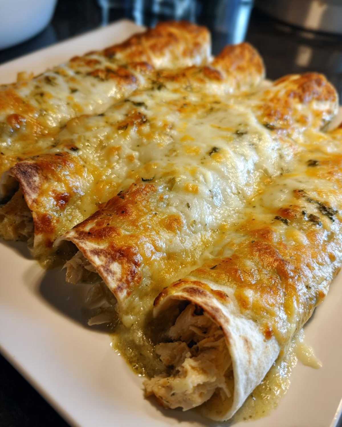 Close-up of three baked green chile chicken enchiladas covered in bubbly, melted cheese.
