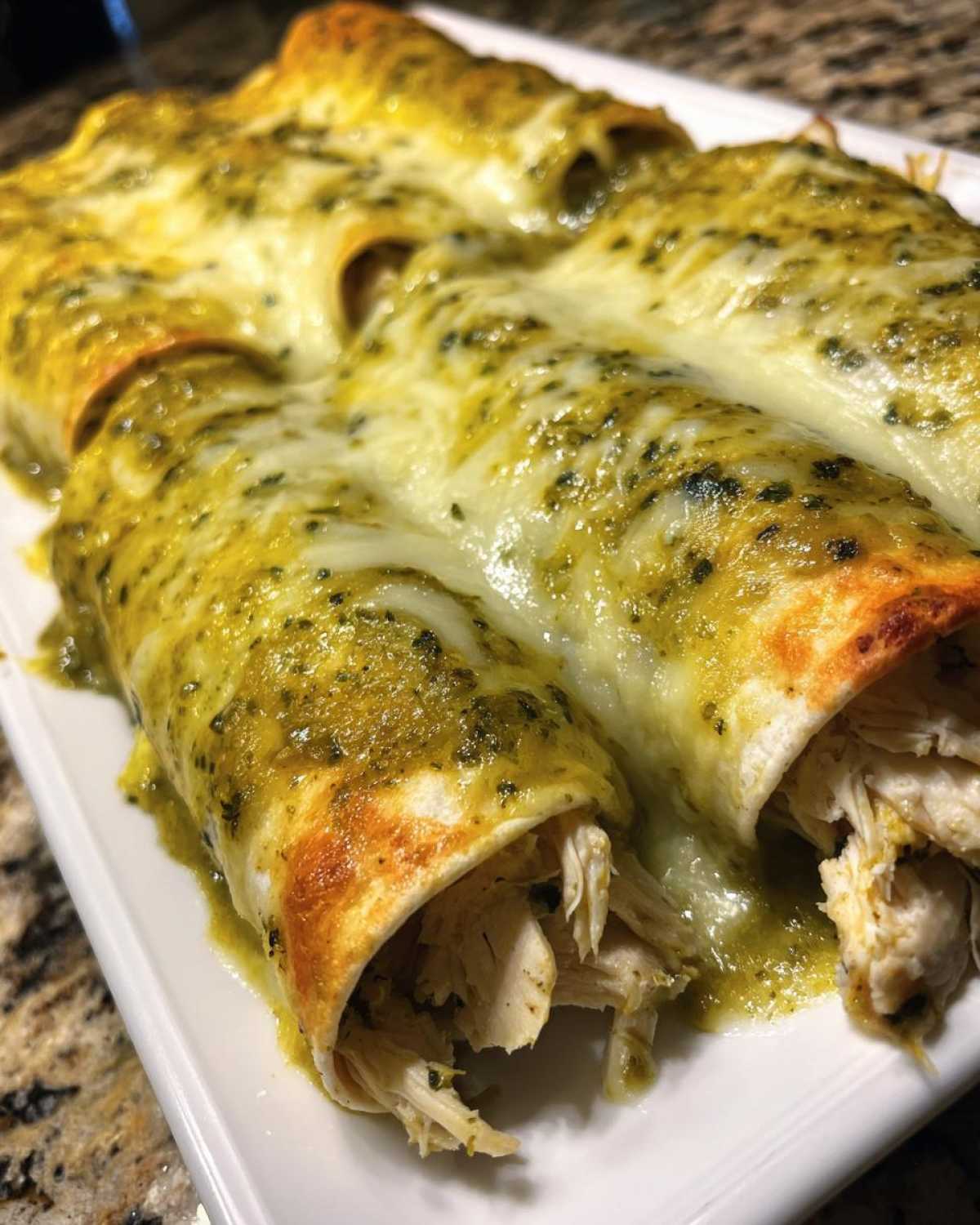 Close-up of baked green chile chicken enchiladas covered in melted white cheese and green sauce.