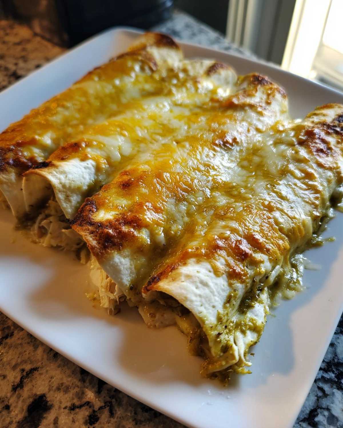 Three baked green chile chicken enchiladas covered in melted, bubbly golden cheese on a white plate.