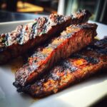 Close-up of three thick, juicy slices of grilled steak coated in a rich Carne asada marinade, resting on a white plate.