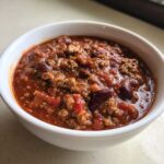 Close-up of a white bowl filled with rich, thick crockpot chili featuring ground meat and kidney beans.