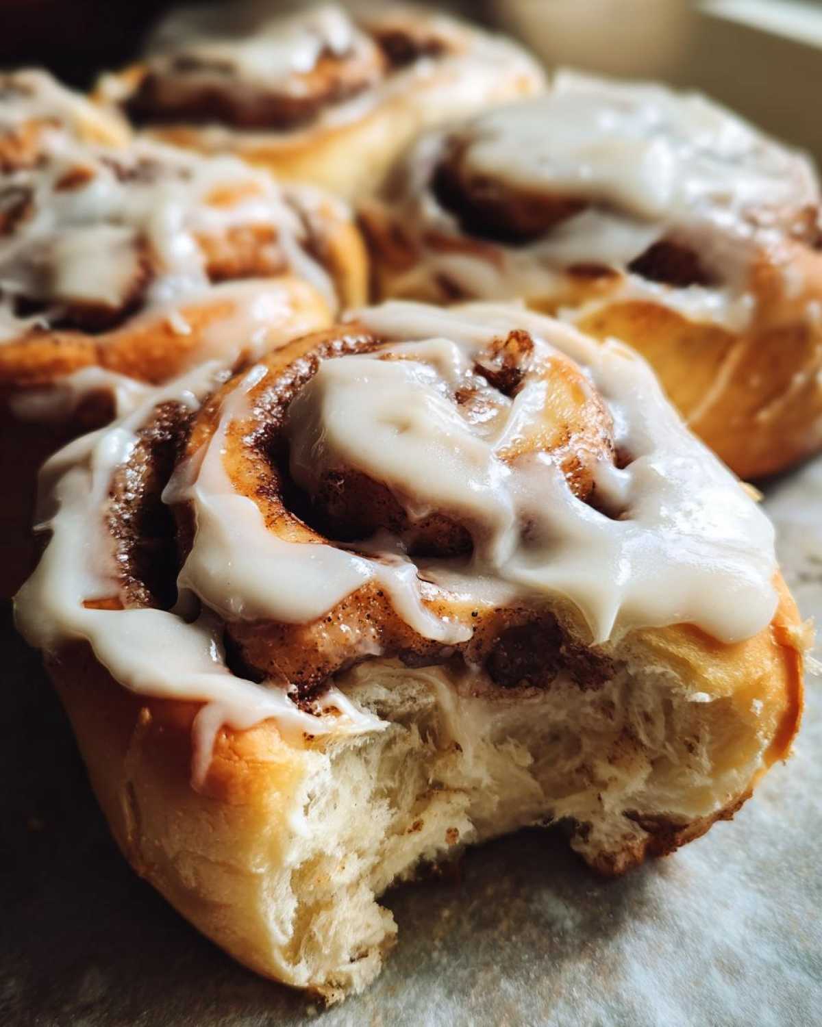 A close-up photo of a fluffy, freshly baked cinnamon roll covered in white icing, with a bite taken out showing the soft interior.