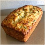 A freshly baked loaf of Italian herb and cheese bread with a golden, cheesy crust and visible green herbs.