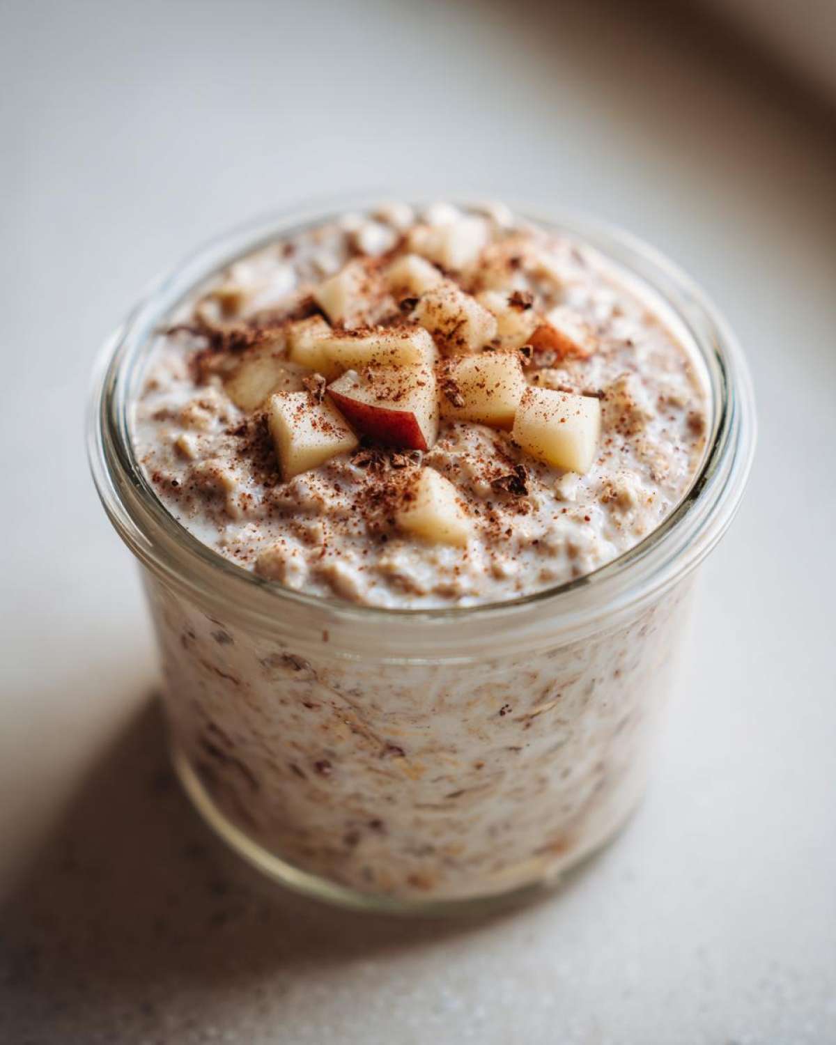 Close-up of apple cinnamon overnight oats in a glass jar, topped with diced apples and a sprinkle of cinnamon.
