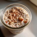 Overhead view of apple cinnamon overnight oats in a glass jar, topped with diced apples and cinnamon.