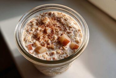 Overhead view of apple cinnamon overnight oats in a glass jar, topped with diced apples and cinnamon.