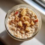 Overhead view of apple cinnamon overnight oats in a glass jar, topped with diced apples and cinnamon.