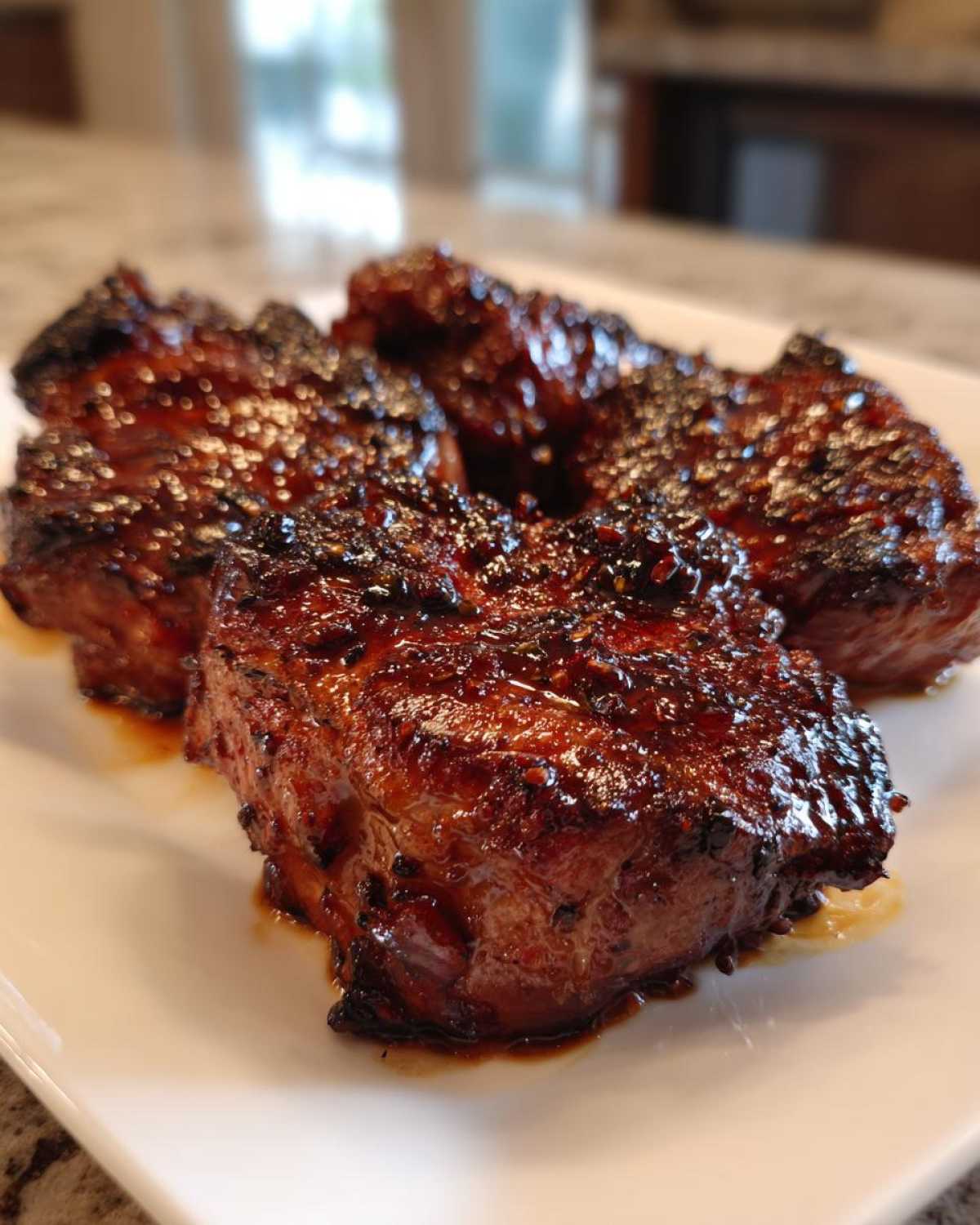 Close-up of four perfectly cooked, glazed pork steak pieces resting on a white plate.