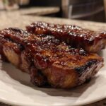 Two pieces of juicy, glazed pork steak resting on a white plate, showcasing a rich, caramelized exterior.