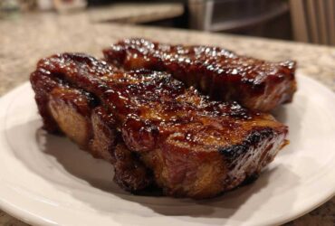 Two pieces of juicy, glazed pork steak resting on a white plate, showcasing a rich, caramelized exterior.
