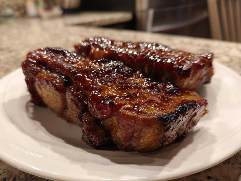 Two pieces of juicy, glazed pork steak resting on a white plate, showcasing a rich, caramelized exterior.