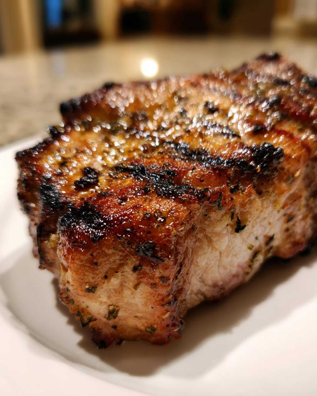 Close-up of a thick, perfectly grilled pork chop showing char marks and herbs from the marinade for pork chops.
