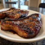 Close-up of two juicy pork steak cuts with a dark, caramelized glaze served on a white plate.