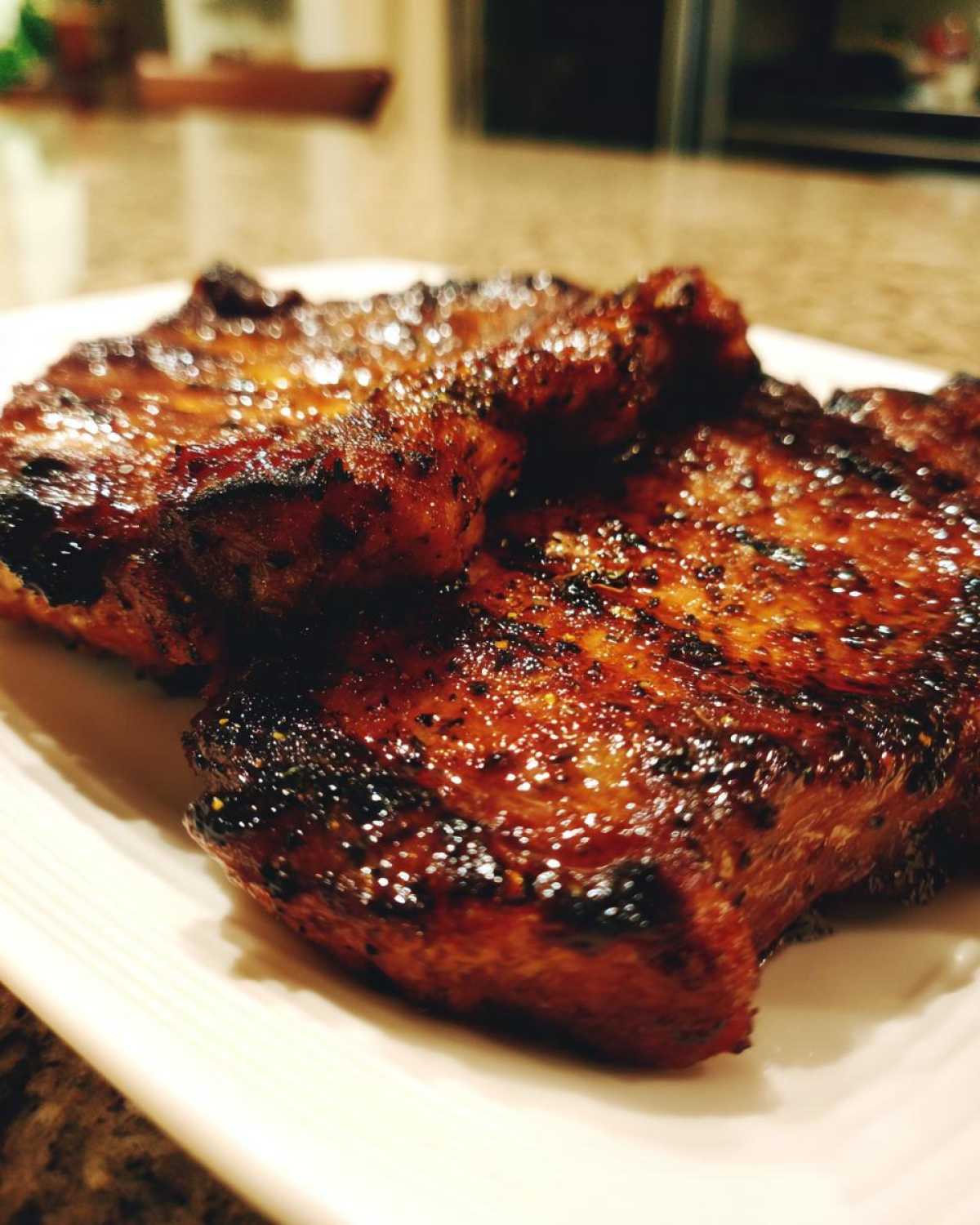 Close-up of two perfectly seared and glazed pork steak cuts on a white plate.
