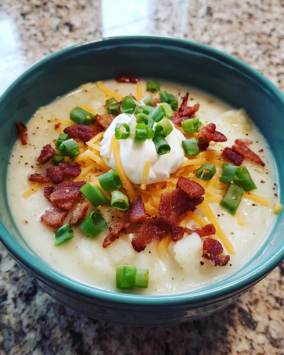 Close-up of a creamy bowl of loaded baked potato soup topped with bacon, cheese, sour cream, and green onions.
