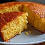 A close-up of a golden slice of buttermilk cornbread with a rich, caramelized top, resting next to the main loaf.