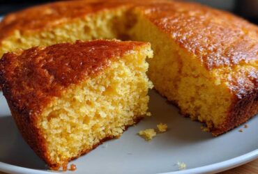 A close-up of a golden slice of buttermilk cornbread with a rich, caramelized top, resting next to the main loaf.