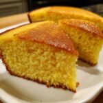 Close-up of moist, golden buttermilk cornbread slices with a shiny, browned top served on a white plate.