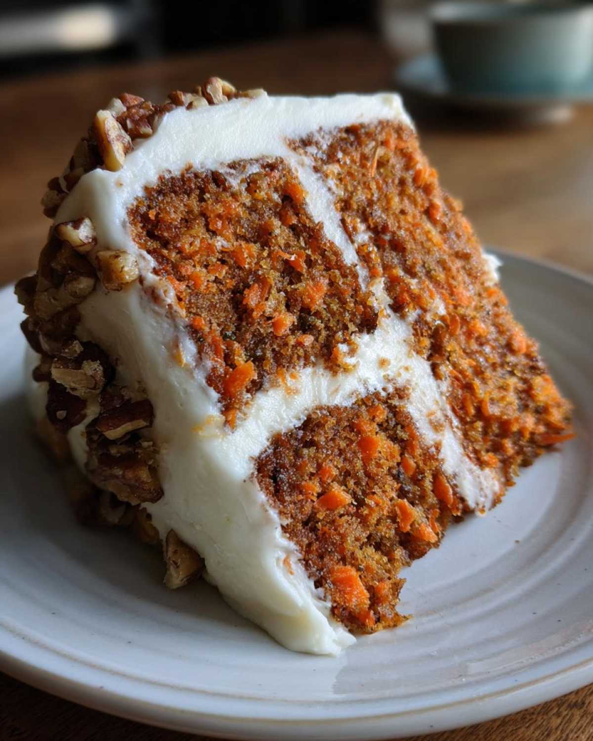 Close-up of a moist slice of carrot cake recipe with thick cream cheese frosting and chopped pecans.