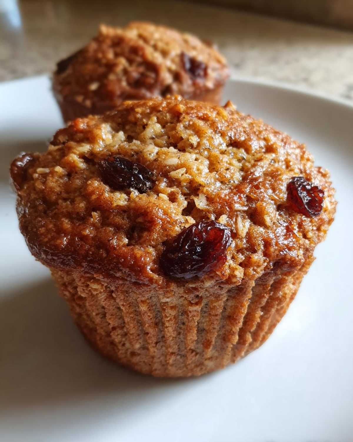 Close-up of a freshly baked, moist honey bran muffin topped with visible raisins and oats.
