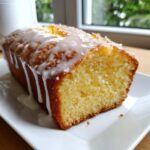 Close-up of a moist lemon pound cake loaf drizzled with white icing, sitting on a white plate.