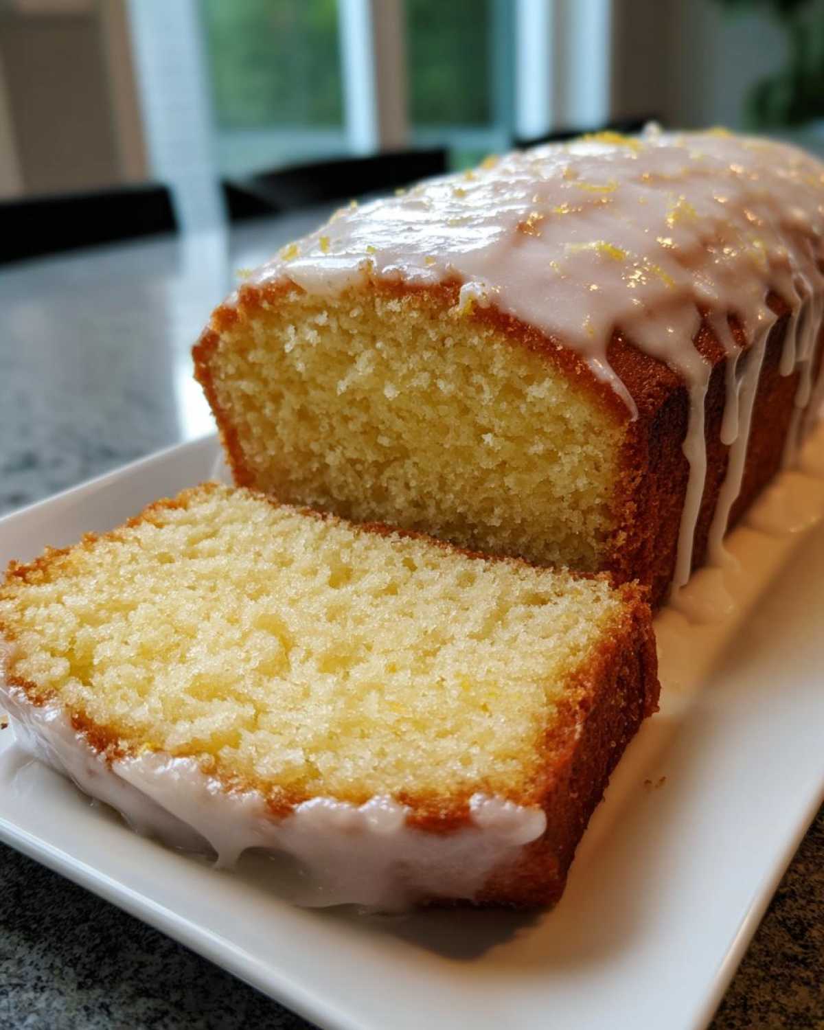 A slice cut from a moist lemon pound cake topped with a white glaze and lemon zest.