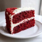 A perfect slice of moist red velvet cake layered with thick white cream cheese frosting.