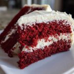 Close-up of a moist slice of red velvet cake layered with thick cream cheese frosting.