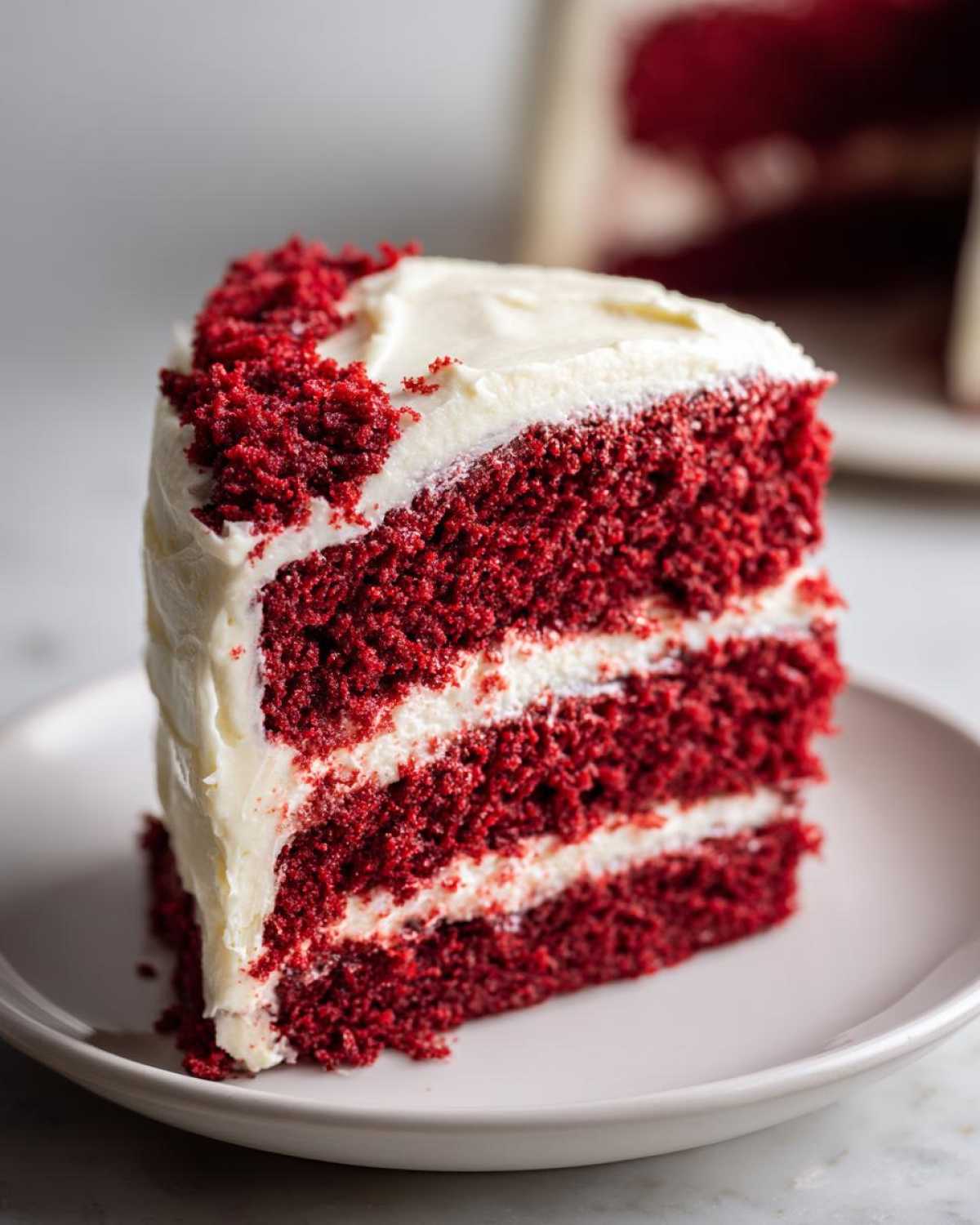 A tall, moist slice of red velvet cake with three layers and thick cream cheese frosting.