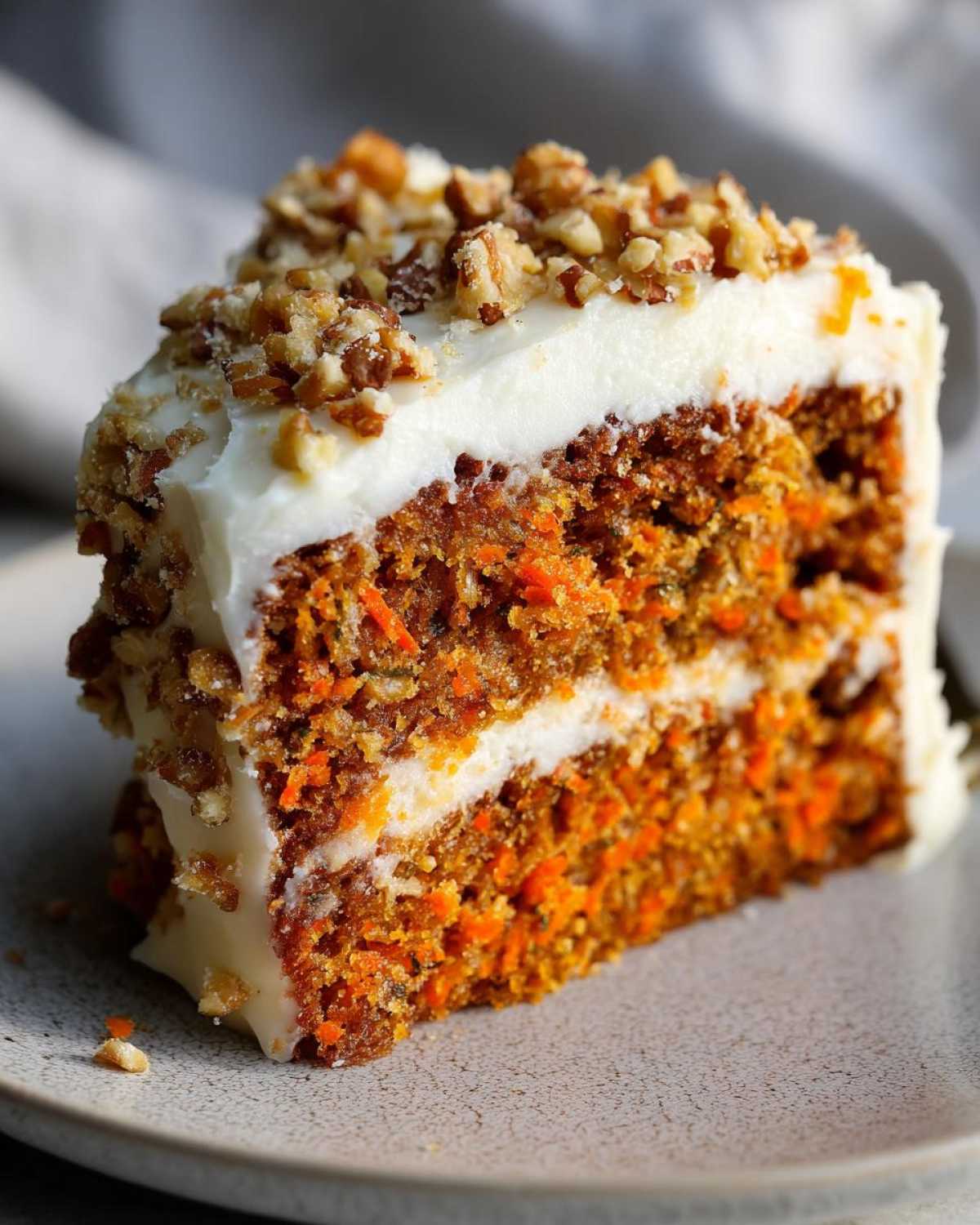 Close-up of a moist slice of carrot cake recipe with thick cream cheese frosting and chopped pecans.
