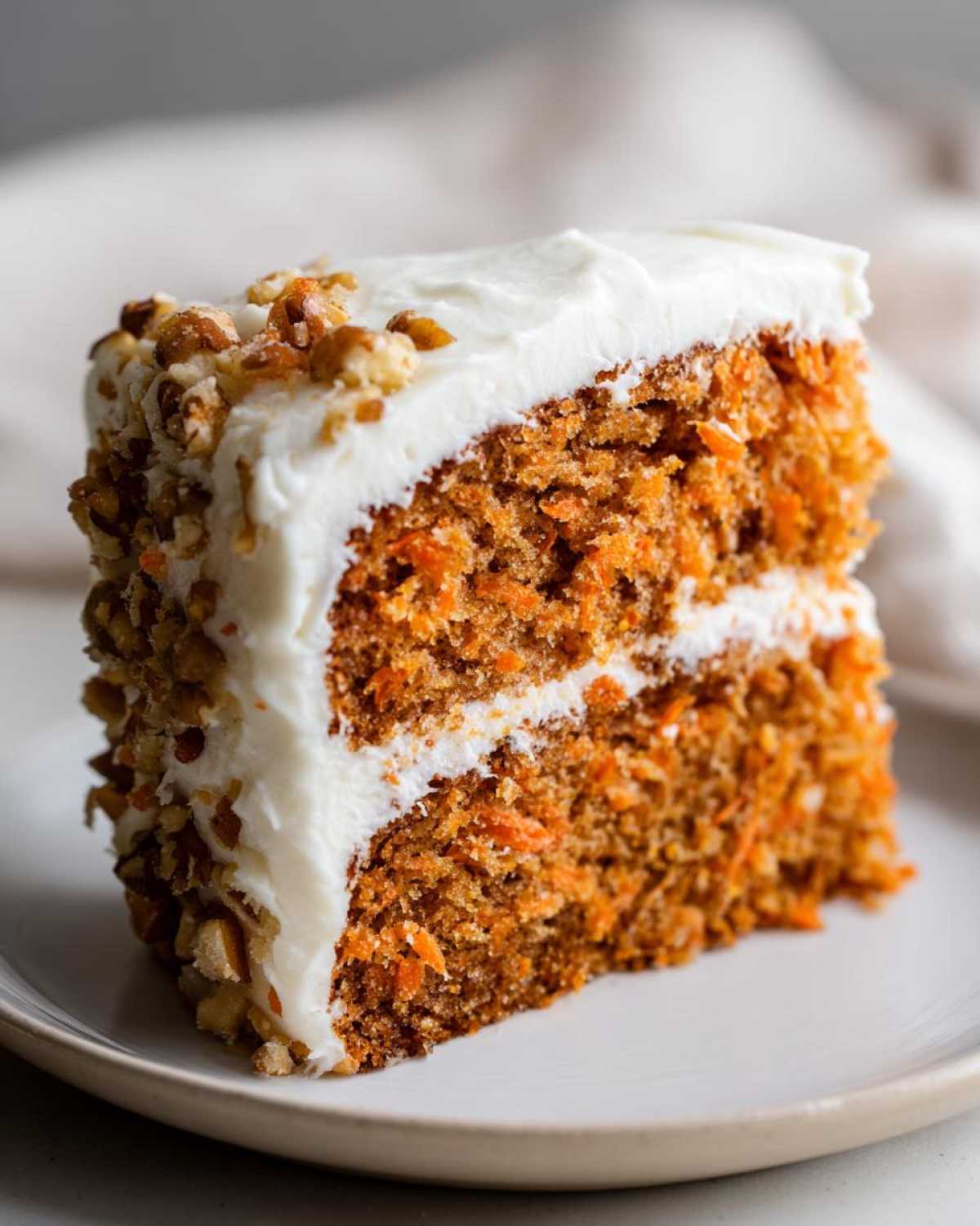 Close-up of a moist slice of carrot cake recipe with thick cream cheese frosting and chopped pecans.