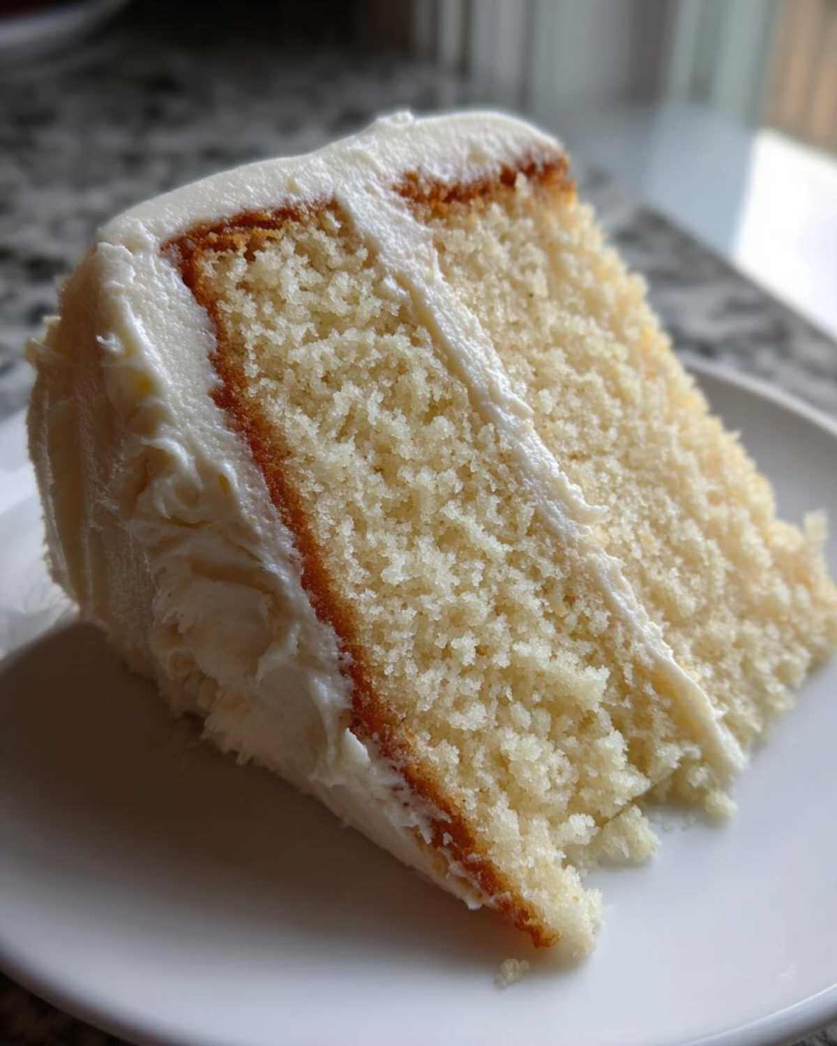 Close-up of a moist slice of vanilla cake recipe with thick white frosting.