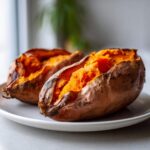 Two perfectly cooked baked sweet potato halves showing bright orange, fluffy insides on a white plate.