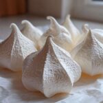 Close-up of several perfectly piped, crisp white meringue cookies resting on parchment paper.