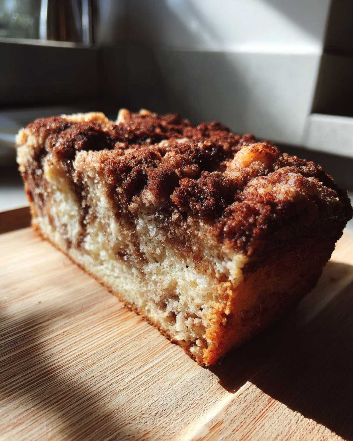 Close-up of a moist slice of coffee cake featuring a thick, dark cinnamon crumb topping.