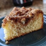 A close-up of a moist slice of coffee cake featuring a thick, sugary cinnamon crumb topping.