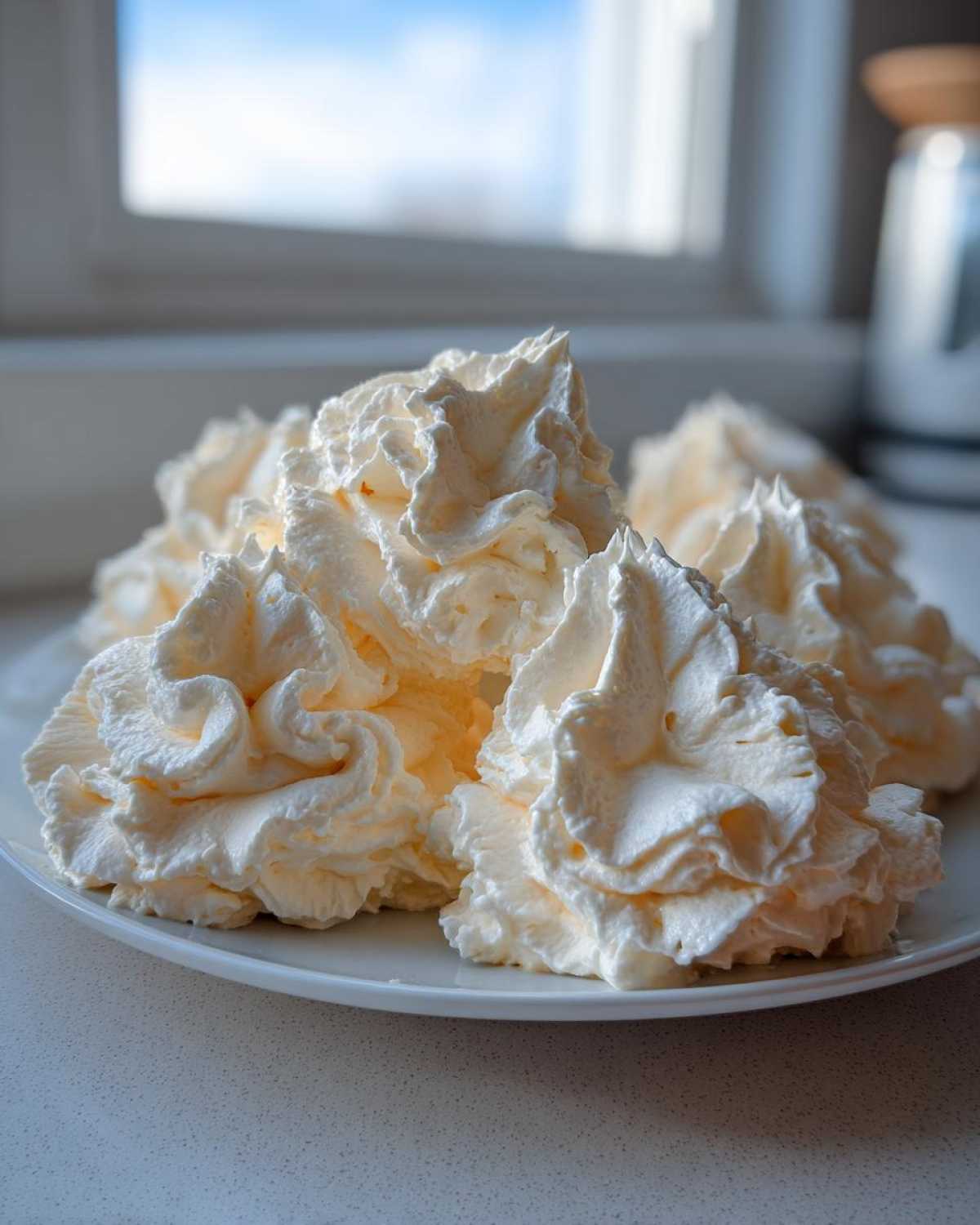 Close-up of several perfectly piped swirls of creamy vanilla buttercream frosting served on a white plate.