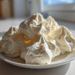 Close-up of piped swirls of light yellow vanilla buttercream frosting served on a white plate.
