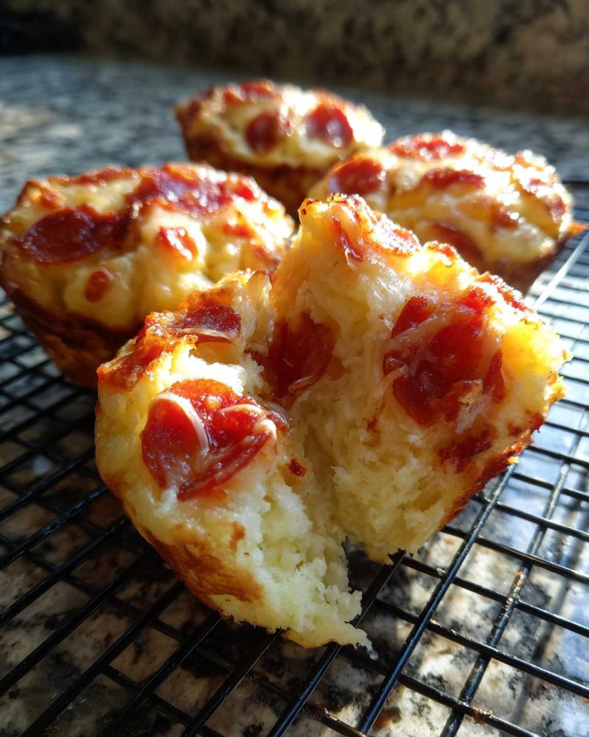 A close-up of one broken Pizza Muffin showing the fluffy interior, topped with melted cheese and pepperoni, resting on a cooling rack.