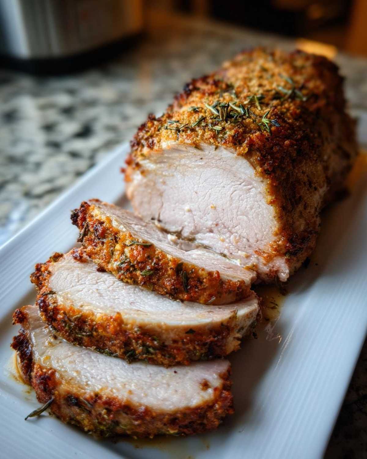 A perfectly cooked pork loin roast, partially sliced, showing the juicy interior and crispy herb crust.