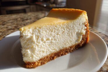 A thick slice of creamy Protein Cheesecake with a graham cracker crust, served on a white plate.