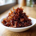 A close-up of a mound of deep brown, glossy caramelized onions served in a small white bowl.