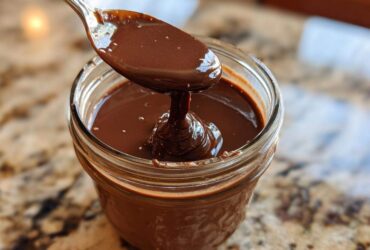 A spoon dripping thick, glossy chocolate sauce into a glass jar, perfect for chocolate overnight oats.