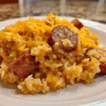 A close-up of a serving of cheesy sausage and rice, featuring sliced smoked sausage mixed throughout the creamy rice.