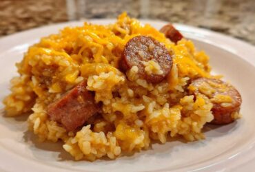A close-up of a serving of cheesy sausage and rice, featuring sliced smoked sausage mixed throughout the creamy rice.