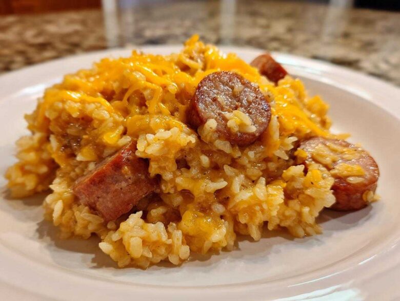 A close-up of a serving of cheesy sausage and rice, featuring sliced smoked sausage mixed throughout the creamy rice.