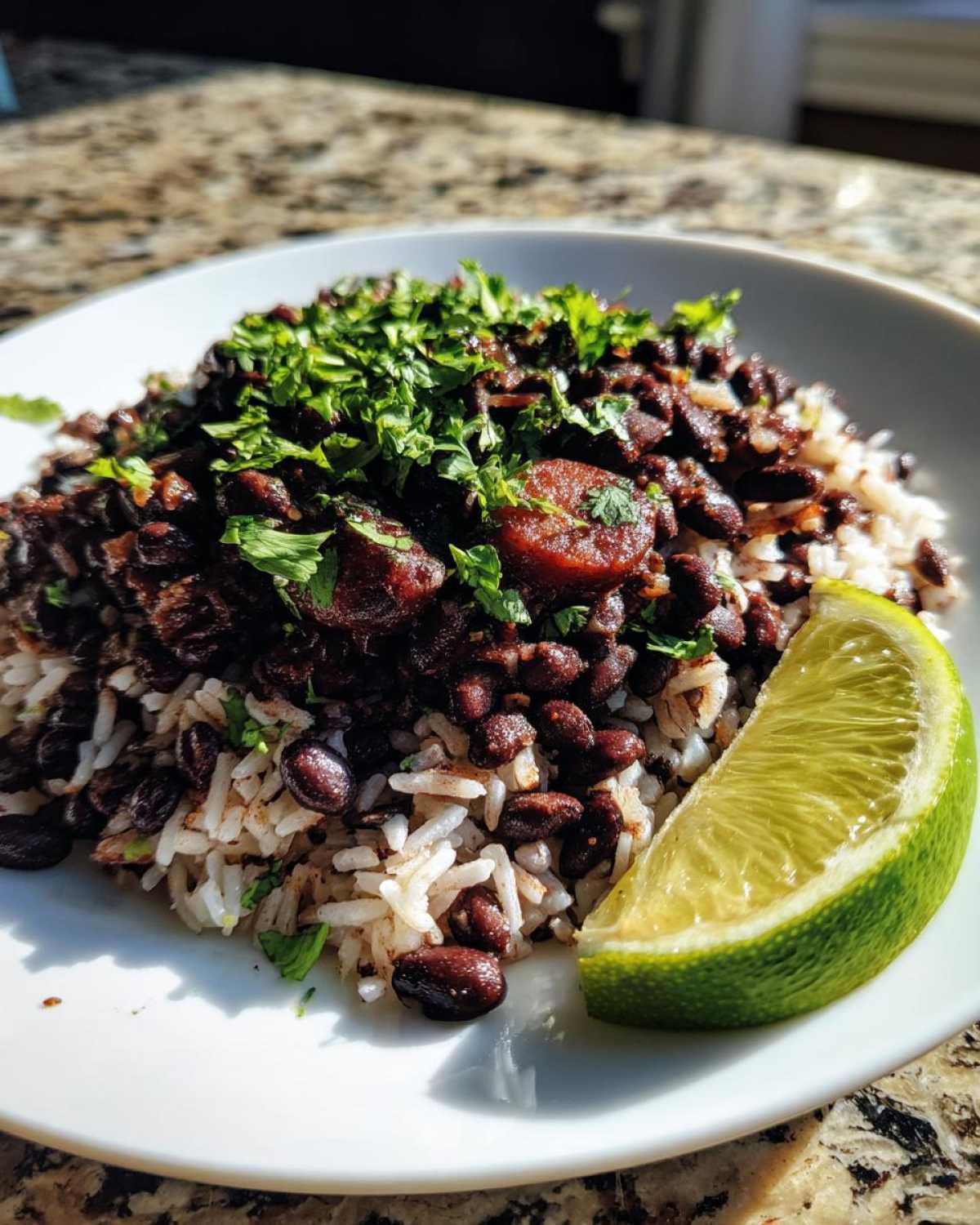 A close-up of a serving of savory black beans and rice topped with fresh cilantro and a slice of lime.