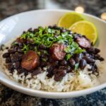 A close-up of savory black beans and rice topped with sliced sausage and fresh cilantro.