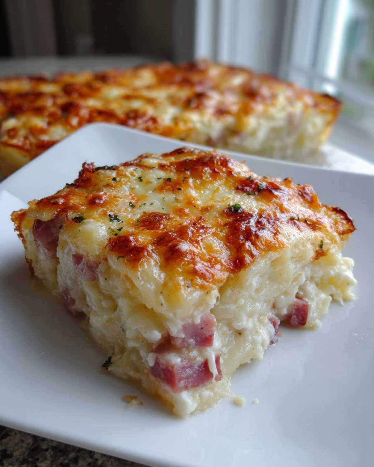 A square serving of creamy scalloped potatoes and ham topped with golden melted cheese.
